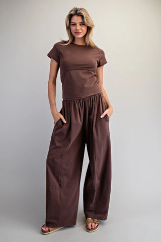 Woman wearing a brown outfit with wide-leg pants on a plain background