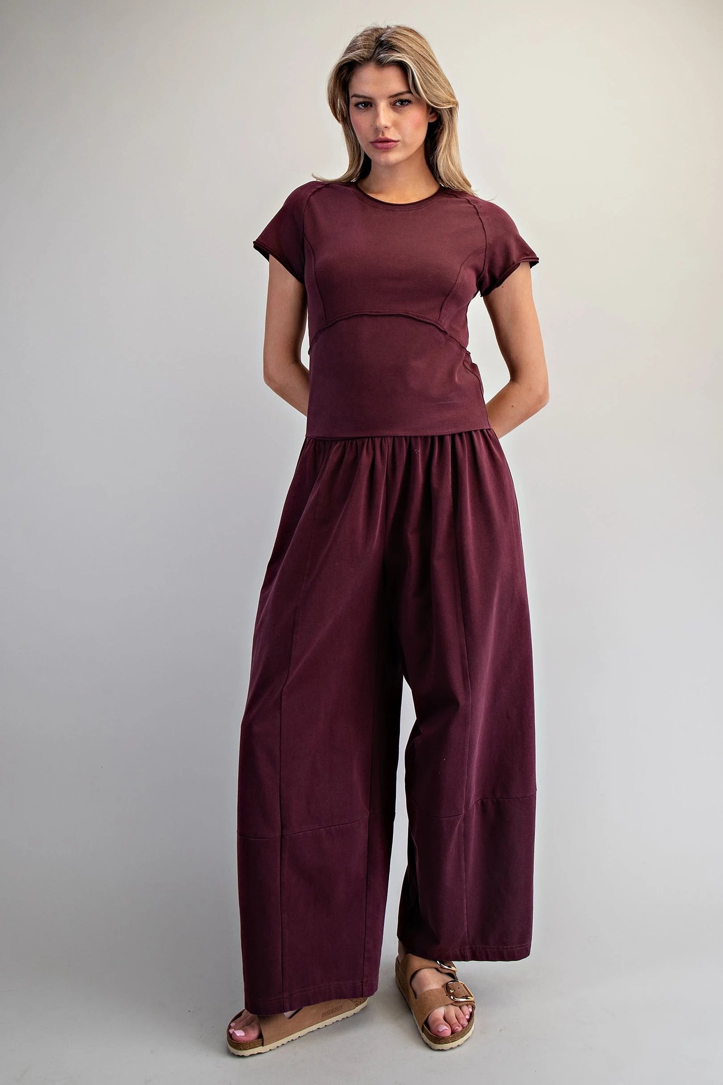 Woman wearing a maroon outfit with wide-leg pants and a top on a plain background