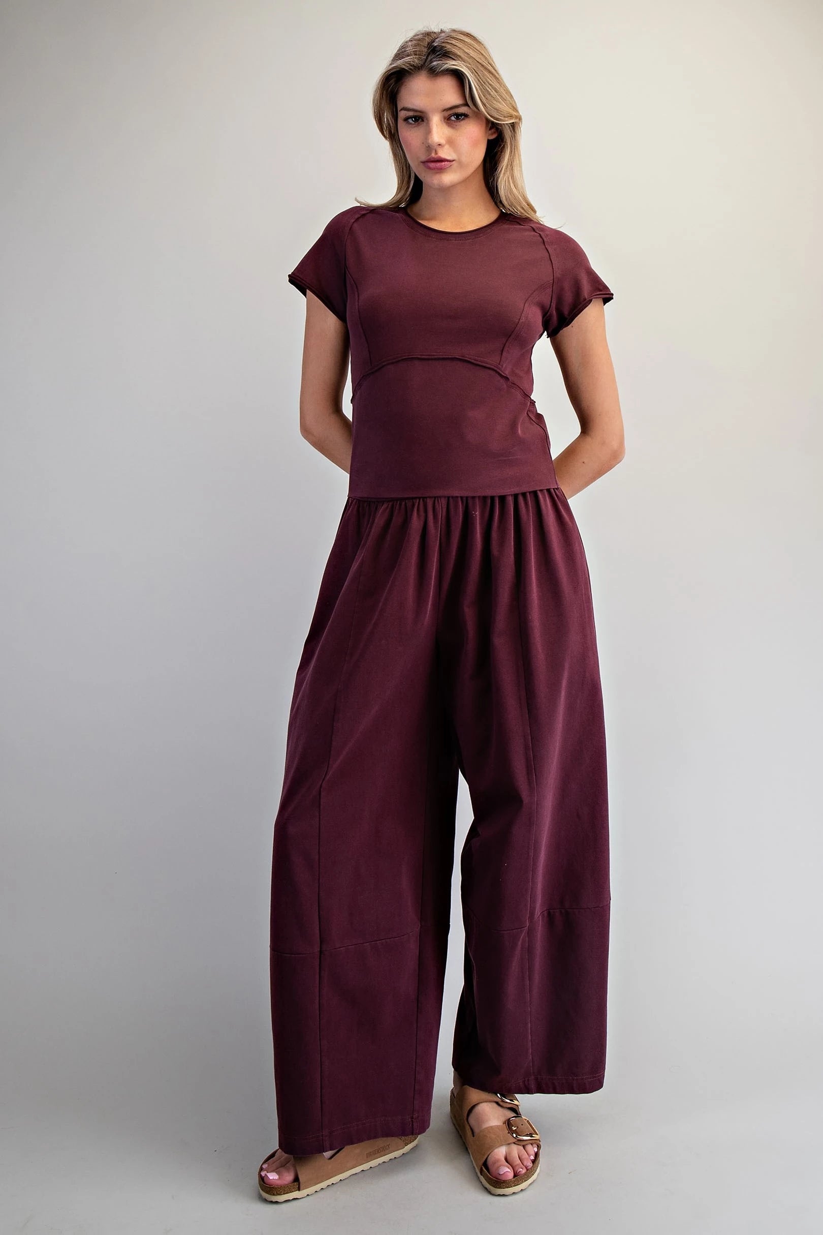 Woman wearing a maroon outfit with wide-leg pants and a top on a plain background