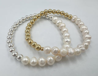 Two pearl necklaces, one gold and silver, the other white, on a light gray background.
