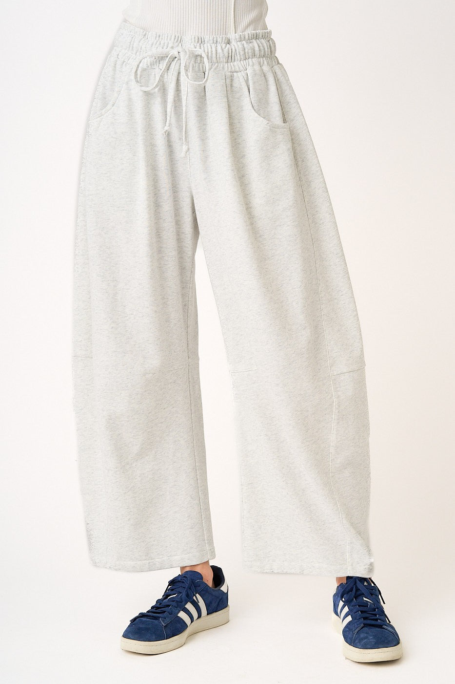 Person wearing light gray sweatpants and blue sneakers on a white background