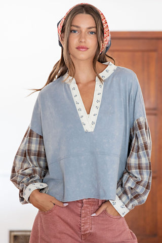 Woman wearing a blue top with plaid sleeves and pink pants, standing indoors.