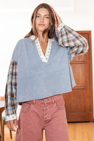 Woman wearing a blue vest over a plaid shirt with pink pants indoors.