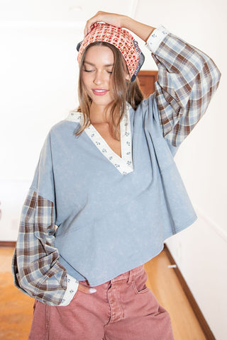 Woman wearing a blue sweater with plaid sleeves and pink pants, holding a patterned headscarf.