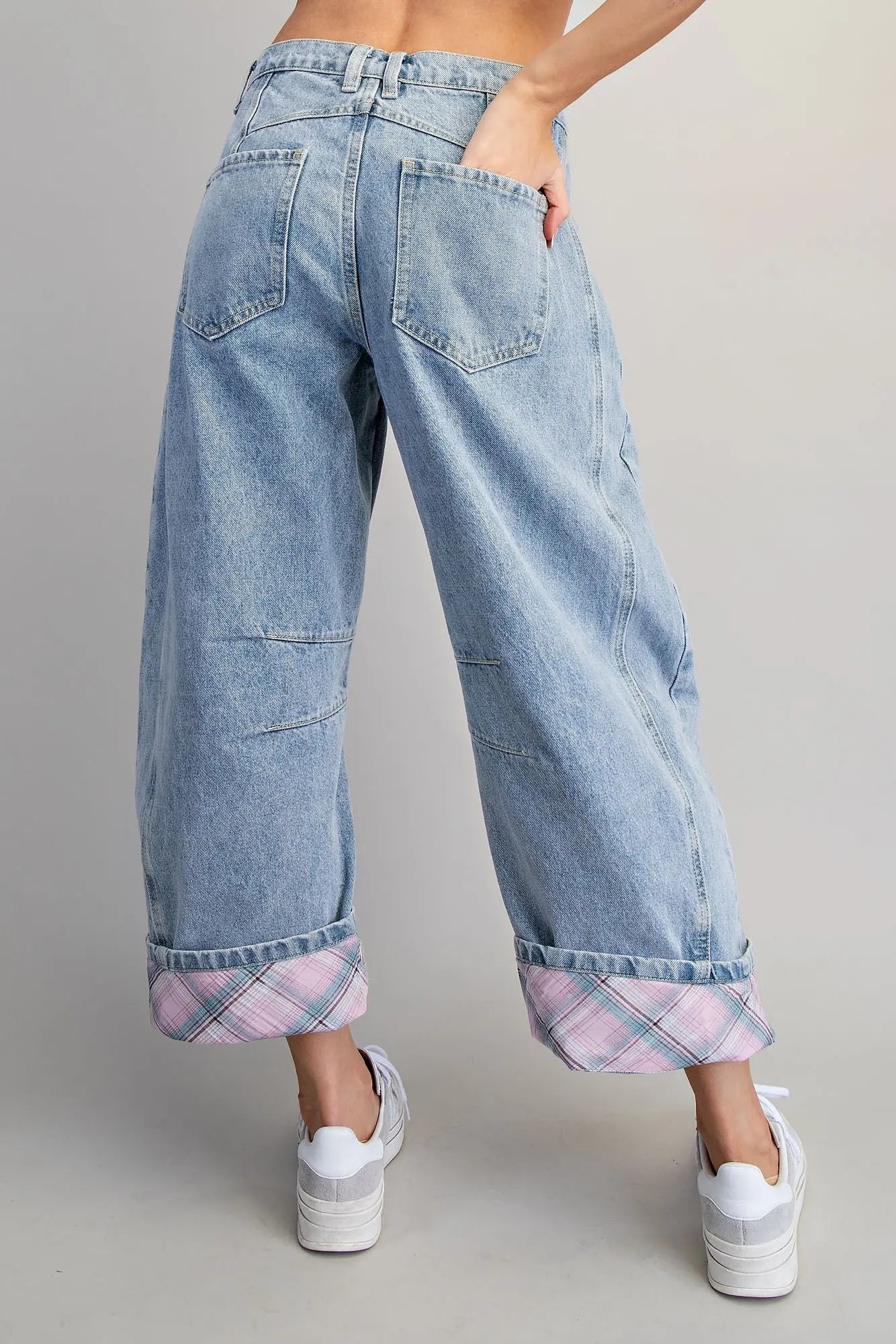 Light blue jeans with plaid cuffs worn by a person on a gray background
