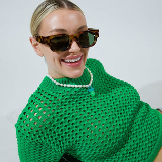 Woman wearing a green sweater and sunglasses against a plain background