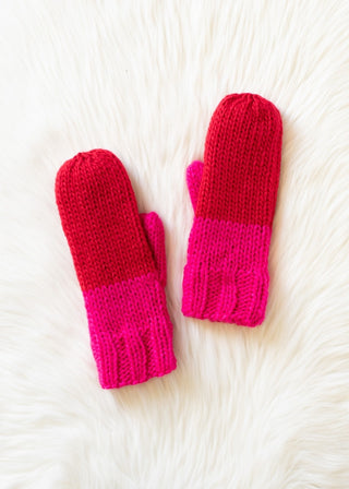 Pair of red and pink mittens on a white textured surface