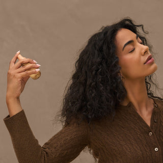 Woman spraying perfume in her hair against a brown background