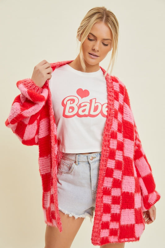 Woman wearing a red and pink checkered cardigan over a white t-shirt with 'Babe' text on a beige background