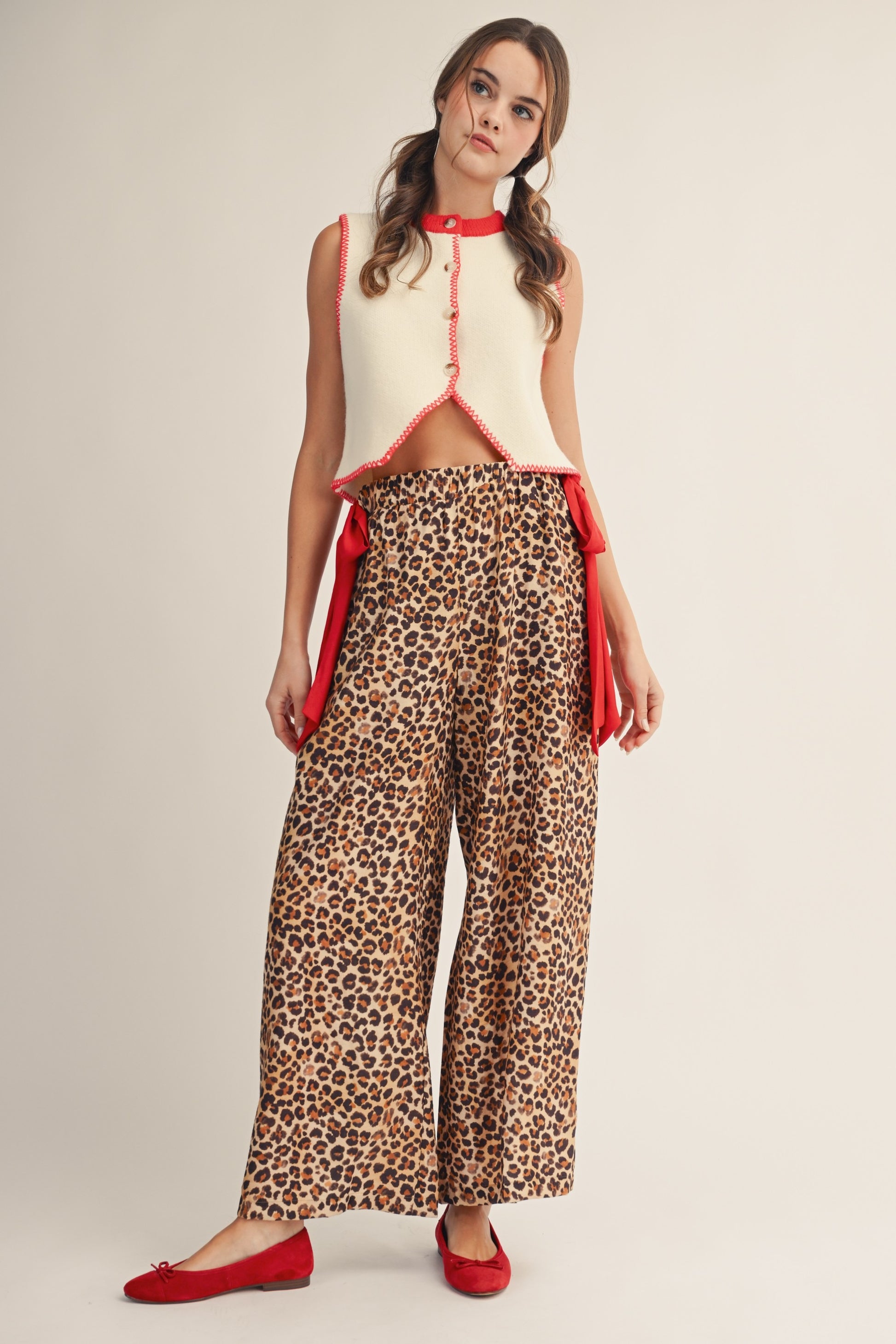 Woman wearing a sleeveless top with red accents and leopard print pants on a beige background
