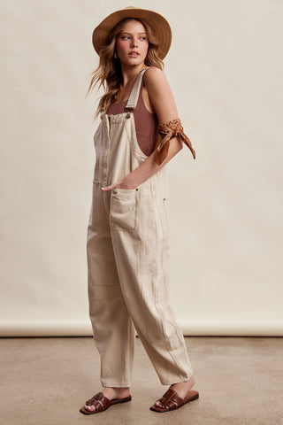 Woman wearing beige overalls and a straw hat on a plain background