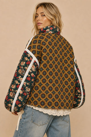 A woman wearing a patterned quilted puffer jacket with floral sleeves, shown from the back against a solid beige background.