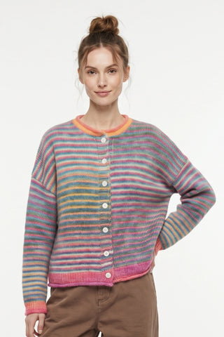 A woman wearing a colorful striped knit cardigan sweater with a button-up front, paired with brown pants, against a plain white studio background.