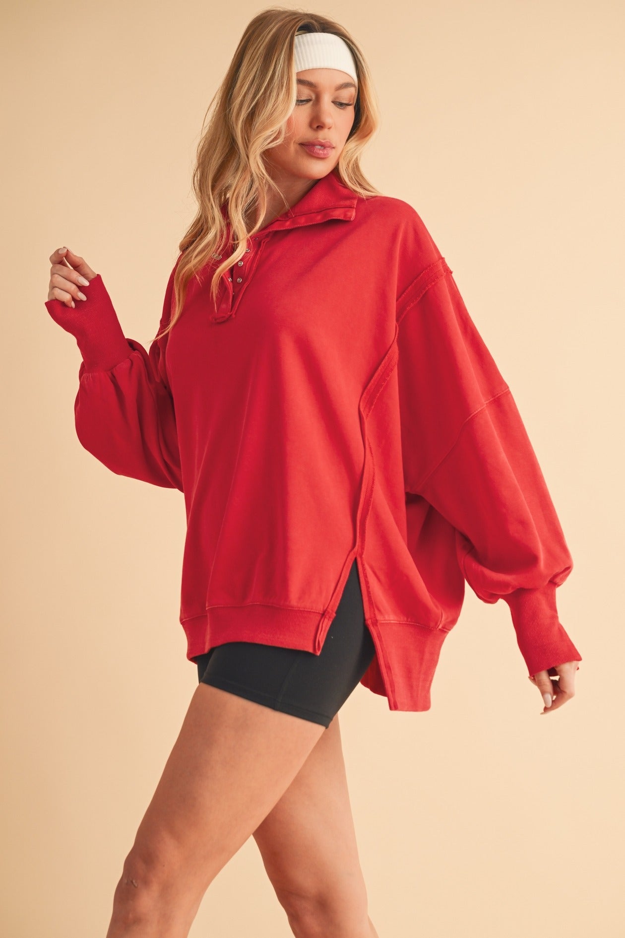 Woman wearing a red oversized sweatshirt and black shorts on a beige background