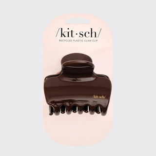 A dark brown recycled plastic claw clip by Kit Sch, mounted on its light pink cardboard retail card against a light gray background.