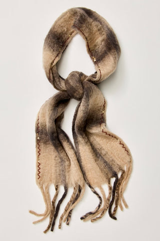 A soft, fuzzy scarf with a mottled beige, brown, and charcoal gray color palette, featuring decorative zigzag stitching and fringed ends, displayed on a light gray background.