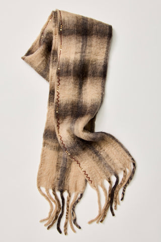 A soft, fuzzy plaid scarf in beige and brown tones, draped elegantly against a light gray background. The scarf features a subtle checkered pattern and decorative zigzag stitching along the edge with small bead accents, finished with fringed ends.