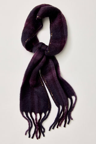 A dark purple gradient knit scarf with gold metallic thread accents and fringed ends, arranged in a loop on a light gray background.