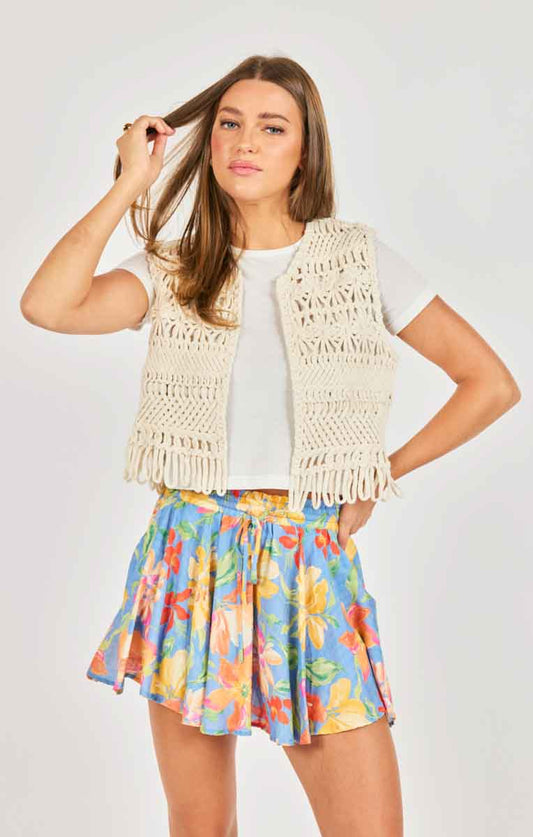 Woman wearing a white crochet vest over a white shirt and colorful floral skirt on a light gray background
