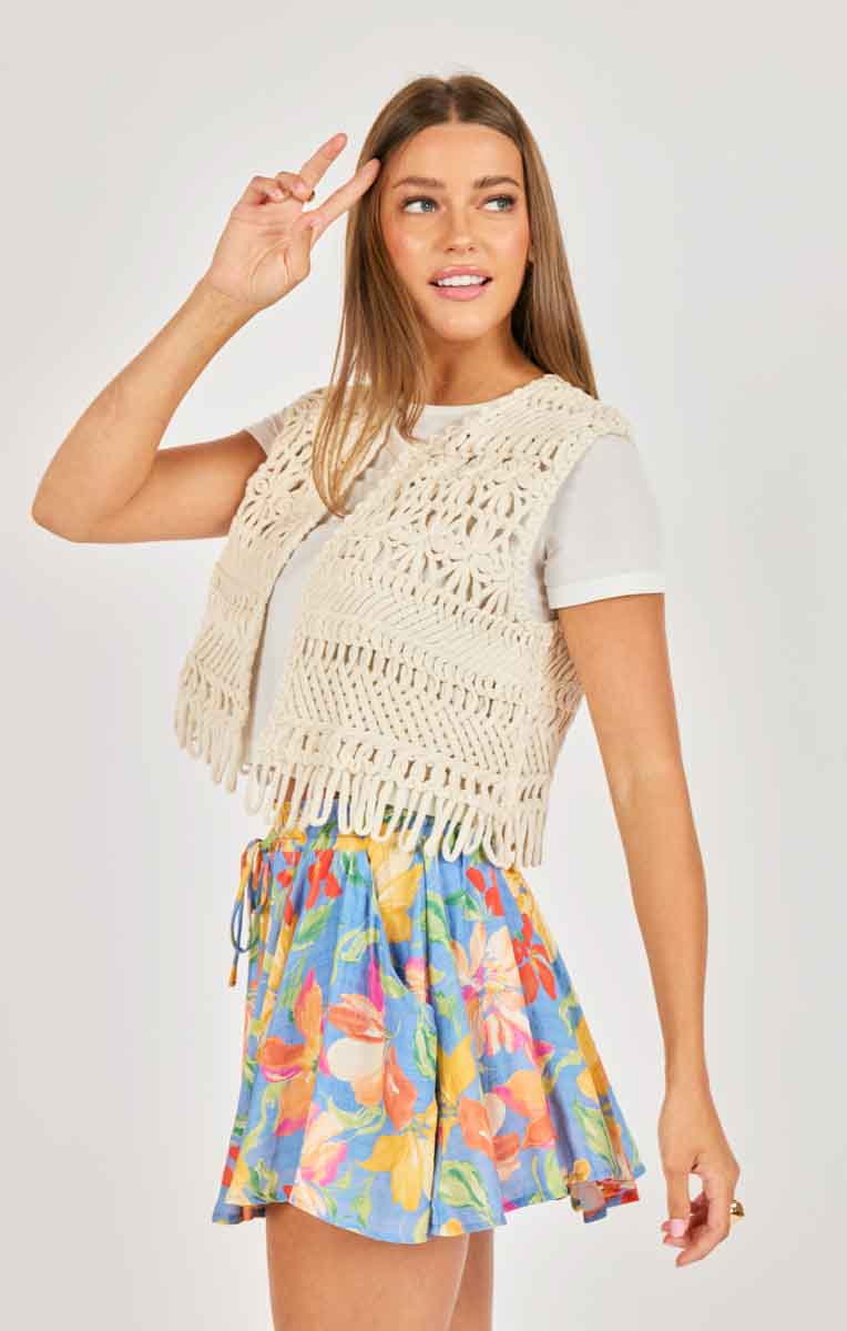 Woman wearing a beige crochet top and colorful floral skirt on a white background