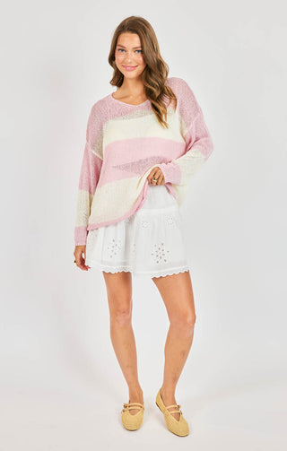 Woman wearing a colorful sweater and white skirt on a plain background
