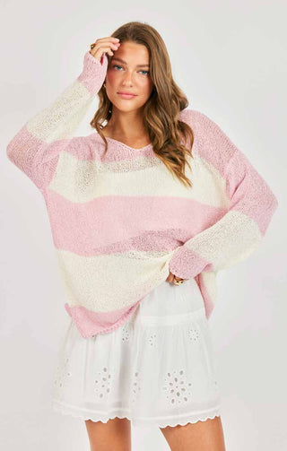 Woman wearing a pastel striped sweater and white lace dress on a light background