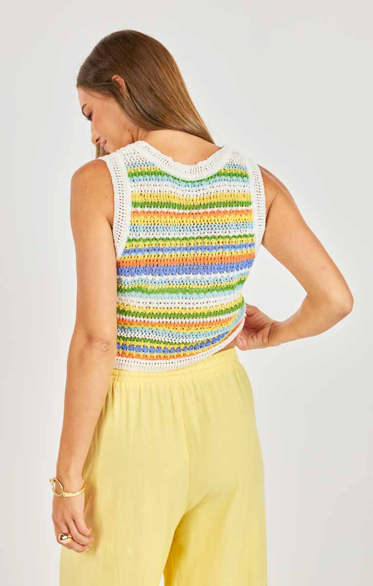 Woman wearing a colorful striped sleeveless top and yellow pants on a white background