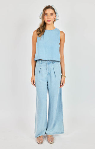 Woman wearing a light blue sleeveless top and wide-leg pants on a white background