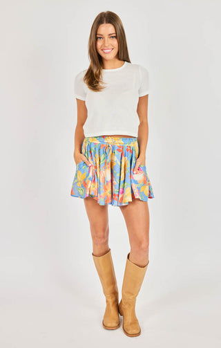 Woman wearing a colorful skirt and white top on a plain background