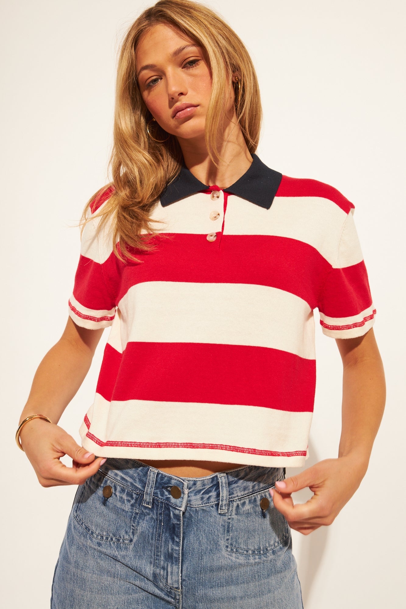 Woman wearing a red and white striped polo shirt with a black collar on a plain background