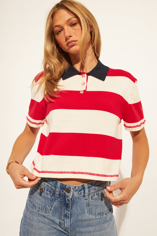 Woman wearing a red and white striped polo shirt with a black collar on a plain background