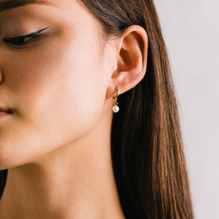 a person wearing a gold hoop earring with a pearl drop