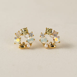 Pair of gold earrings with gemstones and pearls on a beige background
