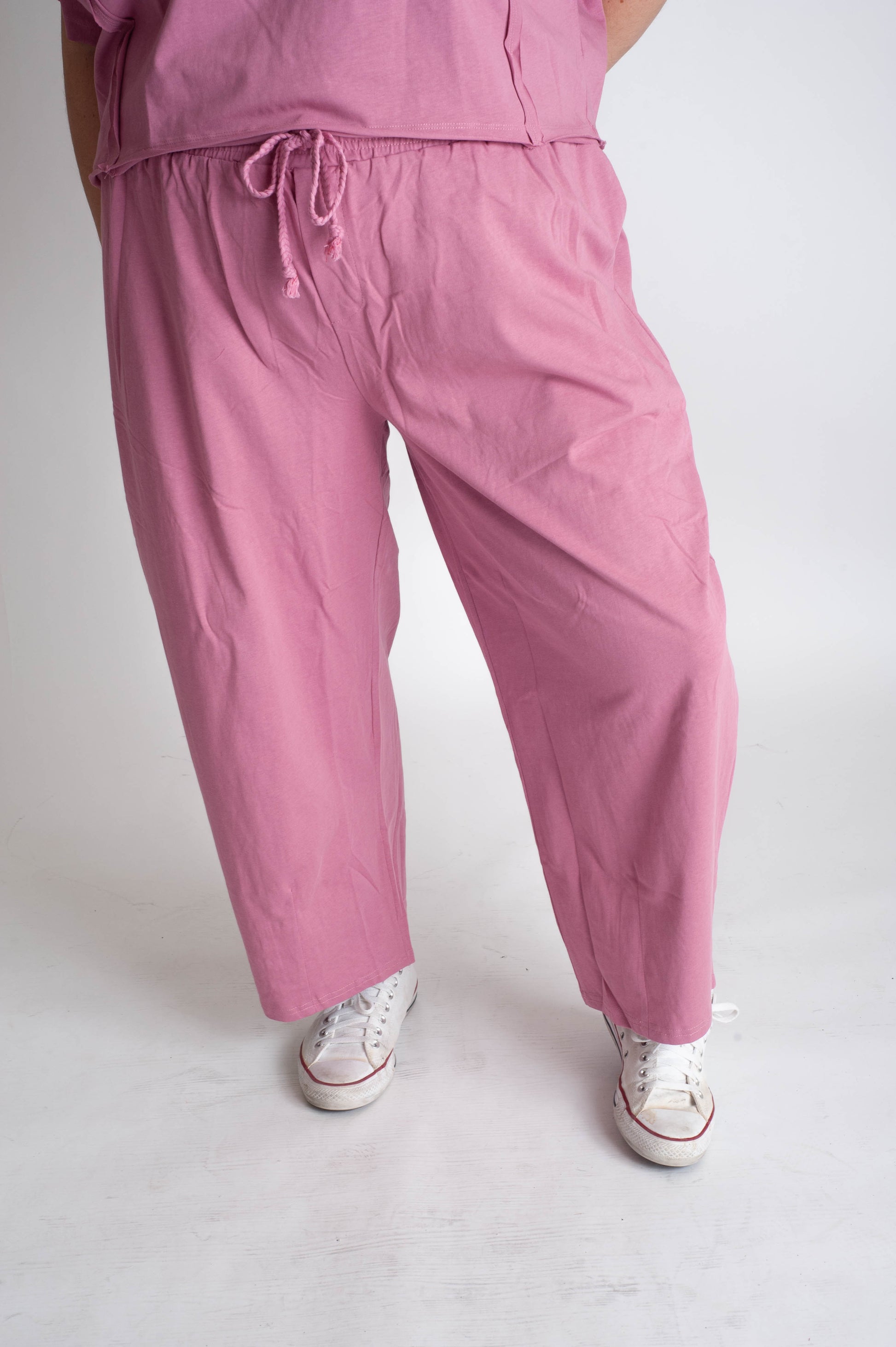 Person wearing pink pants and white sneakers on a plain background