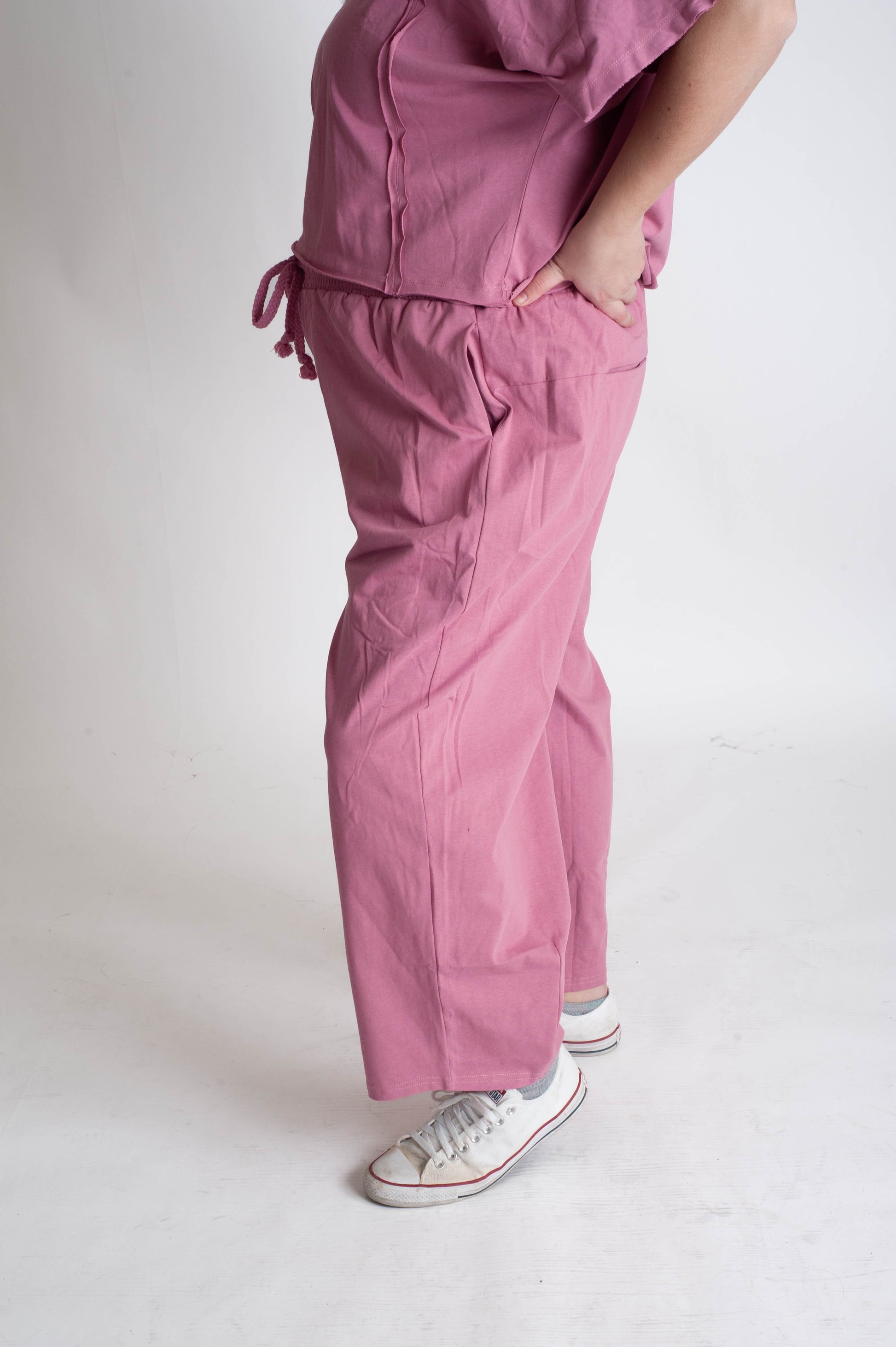 Person wearing pink pants with white sneakers on a plain background