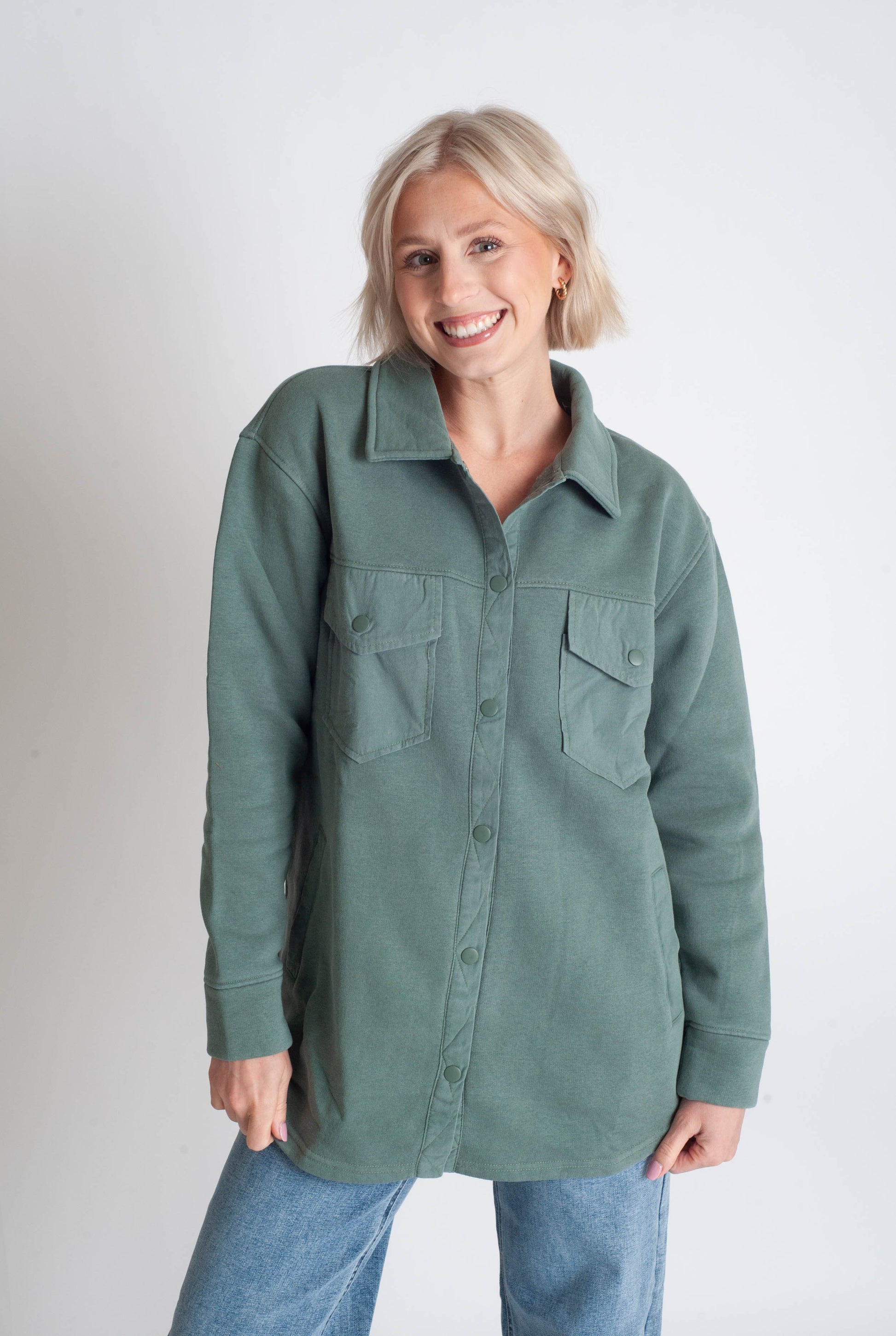 Woman wearing a green button-up shirt and blue jeans on a white background