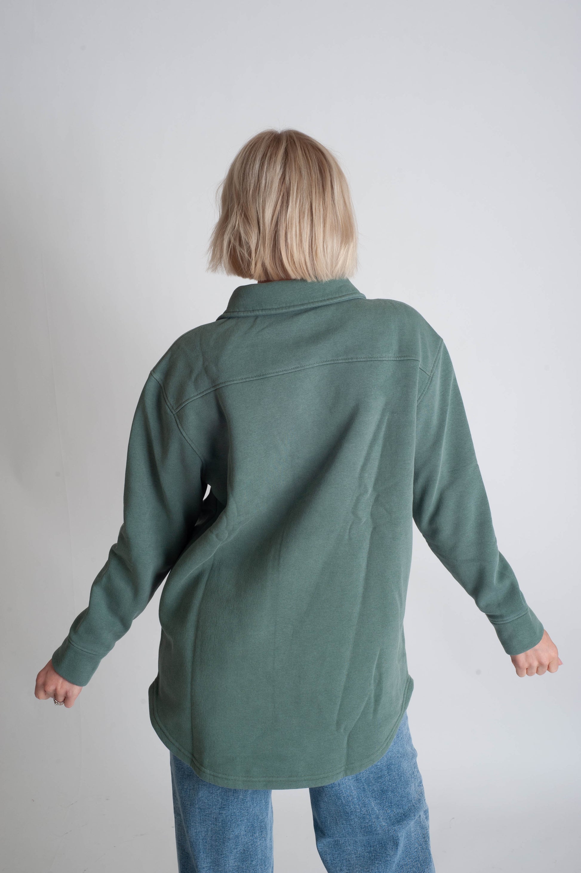 Person wearing a green shirt and blue jeans against a plain background