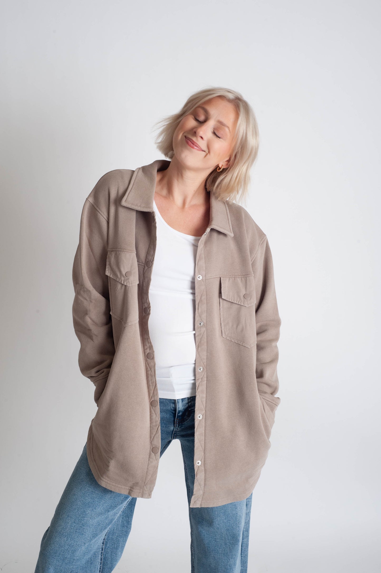 Woman wearing a beige jacket over a white shirt and blue jeans on a white background
