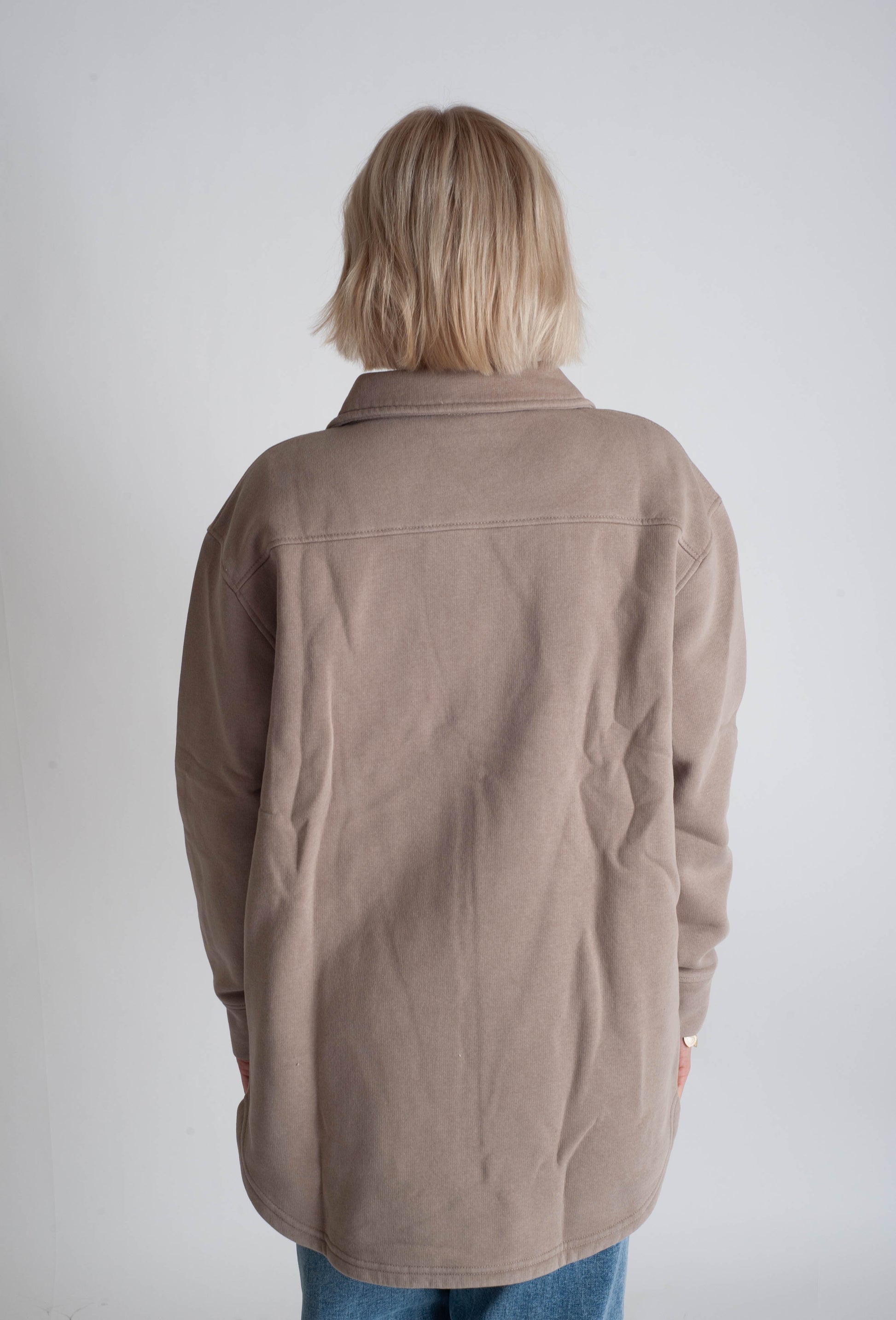 Person wearing a brown jacket from behind on a plain background
