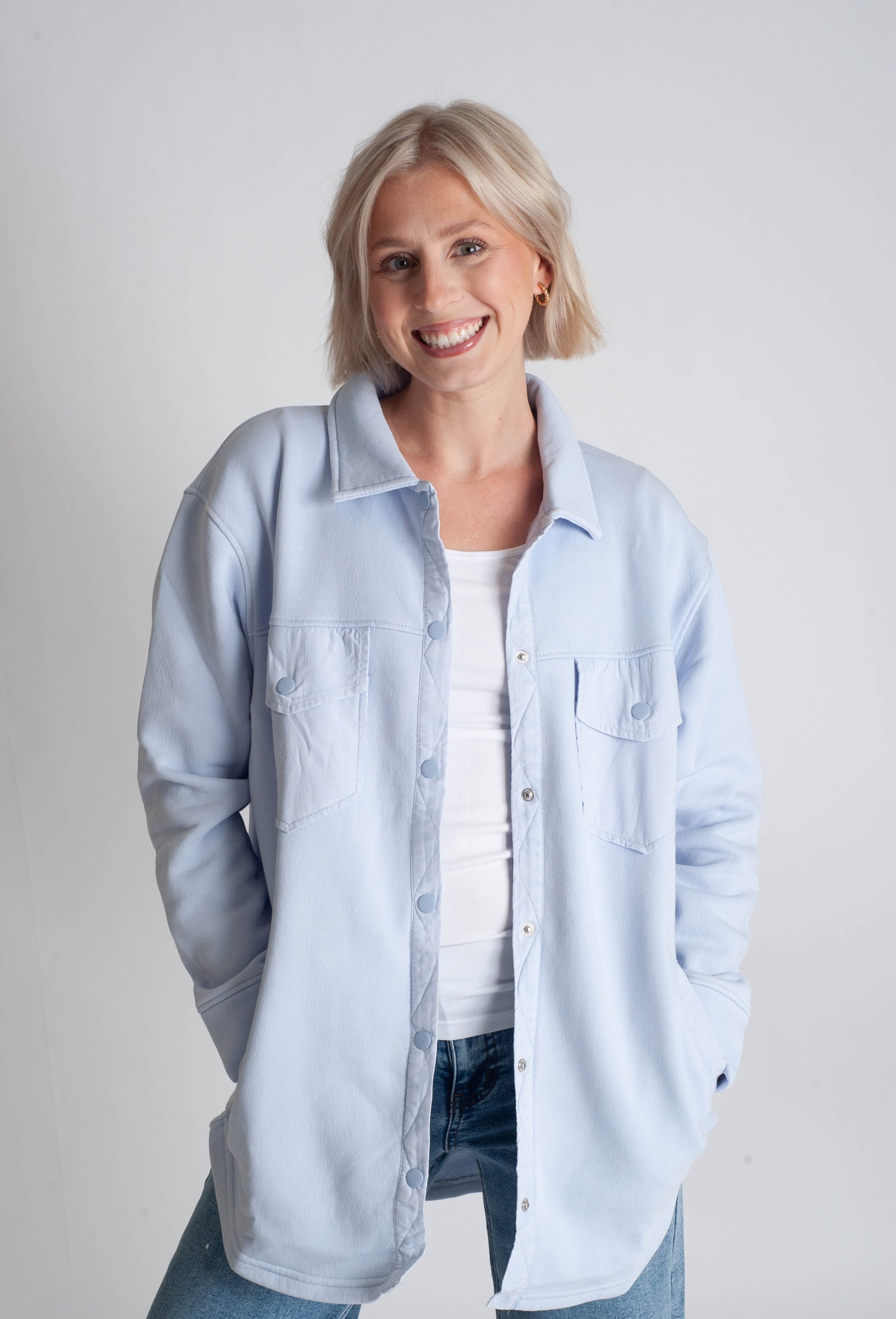 Woman wearing a light blue shirt over a white top on a plain background