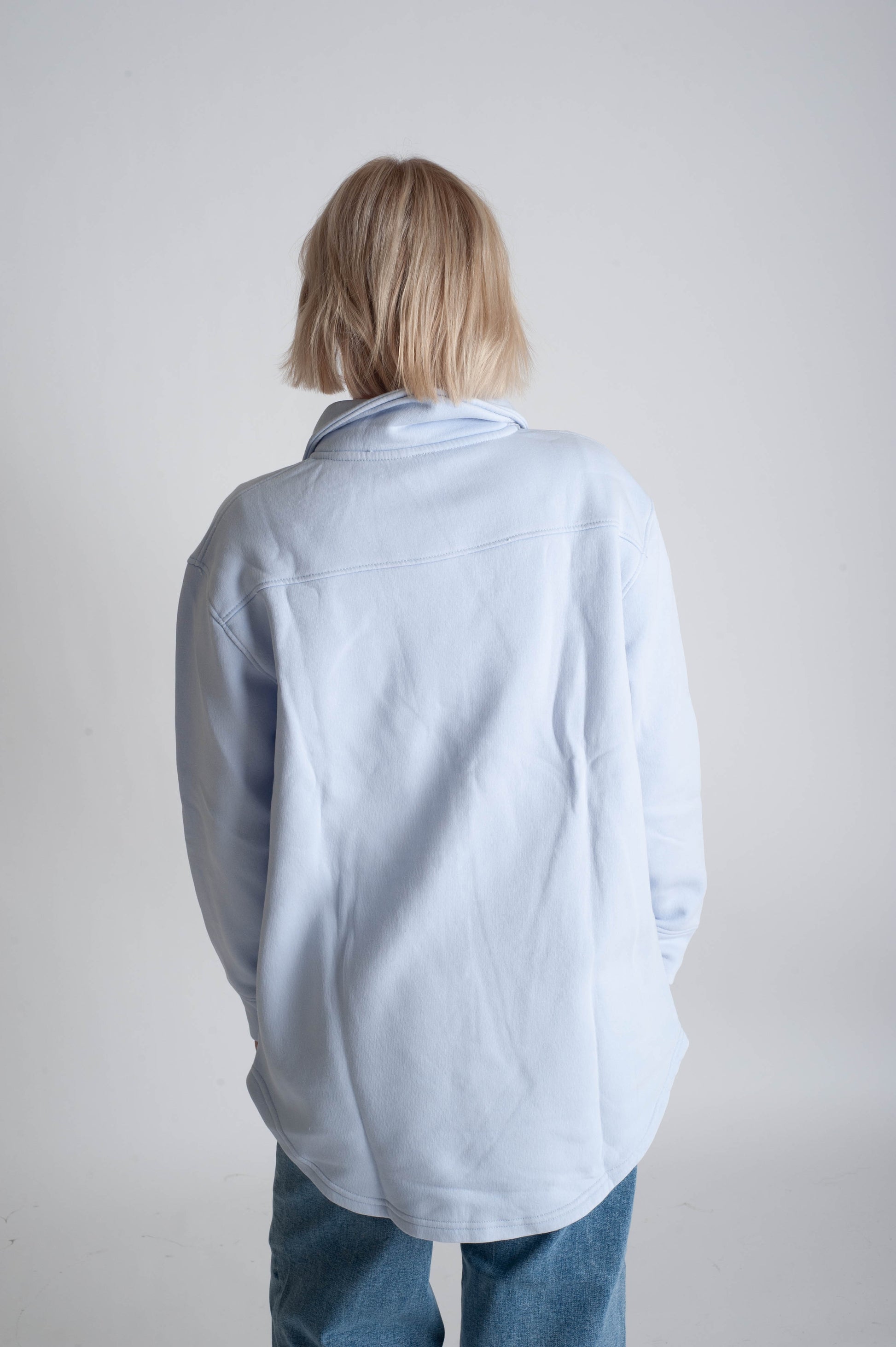 Person wearing a light blue shirt and jeans from behind on a plain background