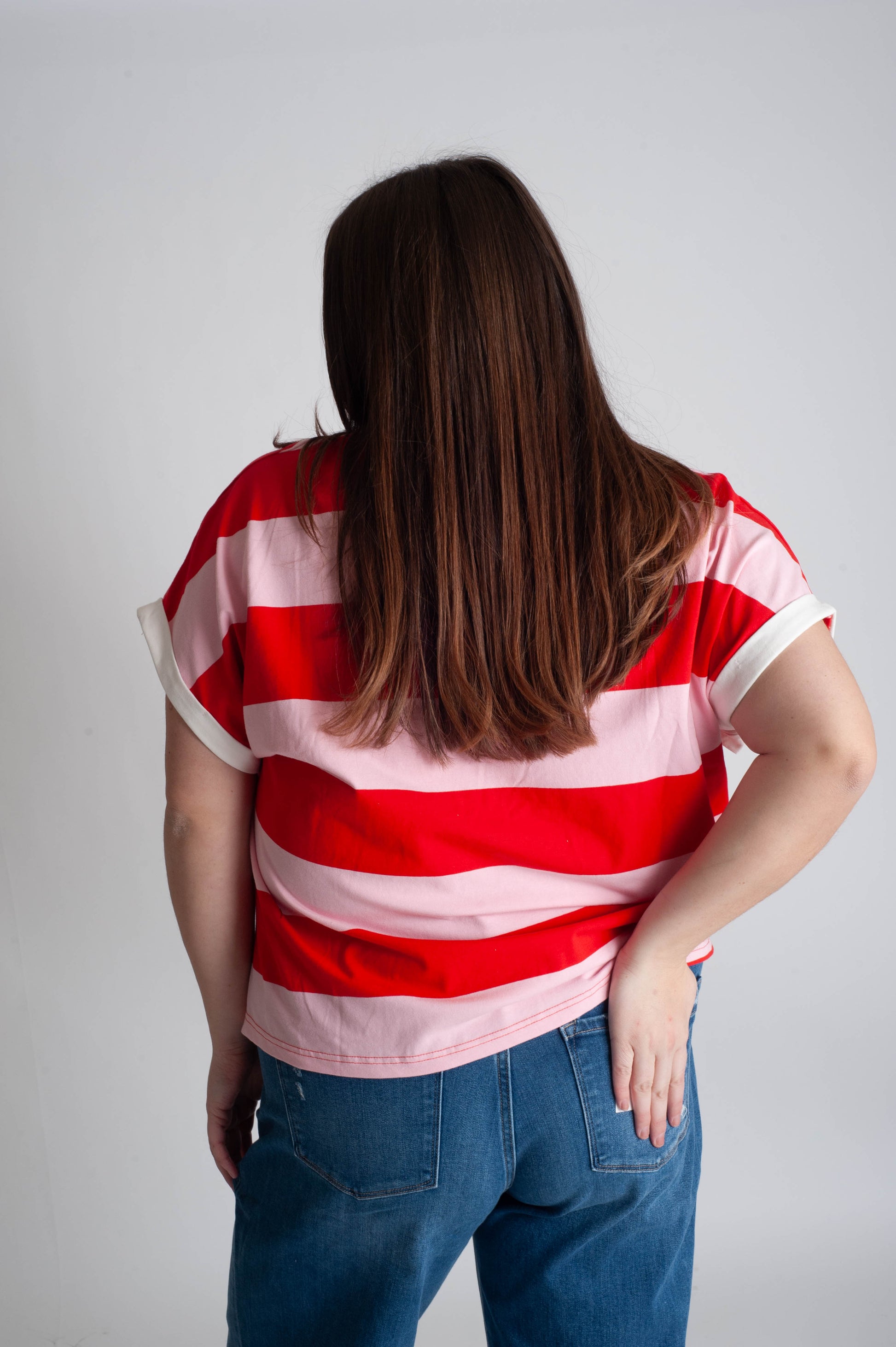Person wearing a red and white striped shirt and blue jeans against a plain background