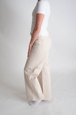 Person wearing beige wide-leg pants and a white shirt on a plain background