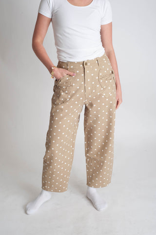 Person wearing beige pants with white polka dots and a white top on a plain background
