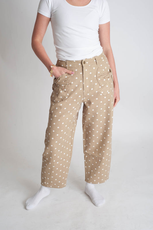 Person wearing beige pants with white polka dots and a white top on a plain background