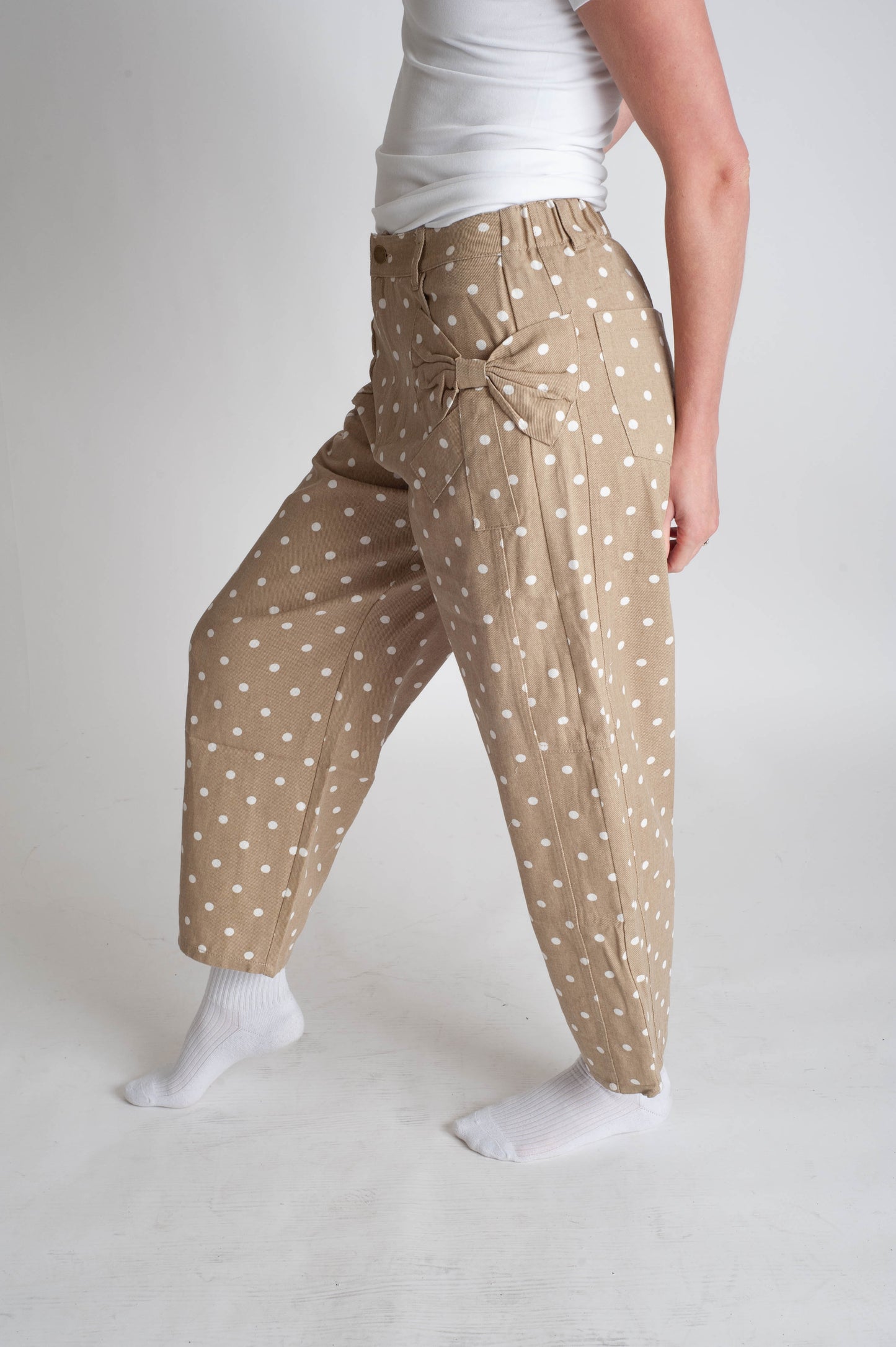 Person wearing beige pants with white polka dots on a plain background