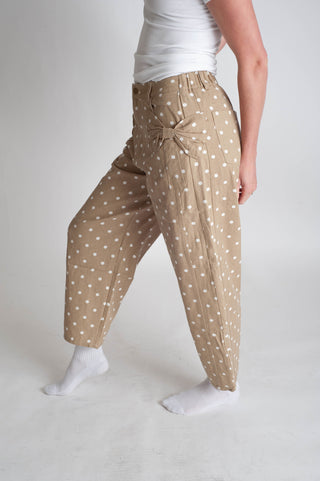 Person wearing beige pants with white polka dots on a plain background