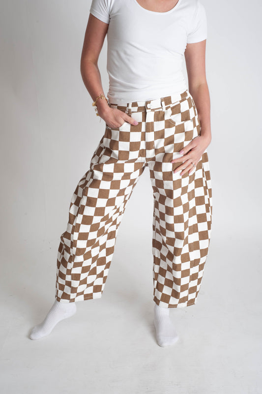 Person wearing a white t-shirt and checkered brown and white pants on a plain background