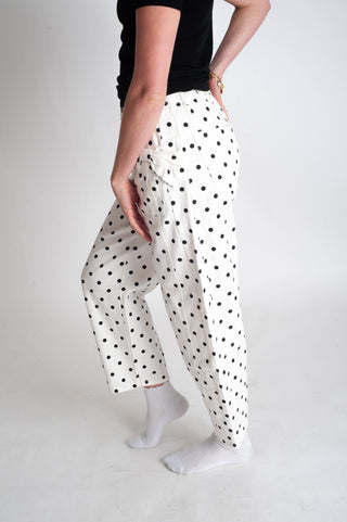 Person wearing white pants with black polka dots on a plain background