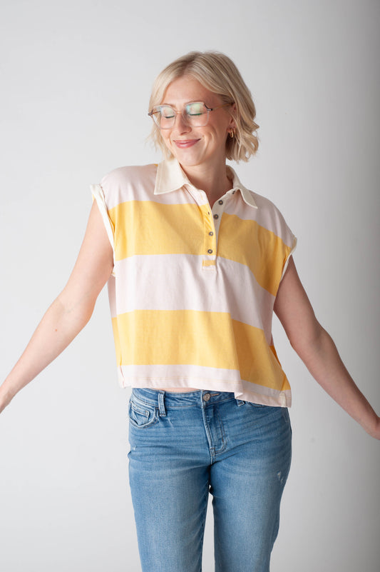 Woman wearing a yellow and pink striped shirt with blue jeans on a plain background